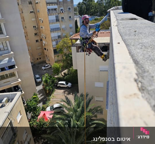 אדם תלוי על חבל עם ציוד בטיחות על בניין
